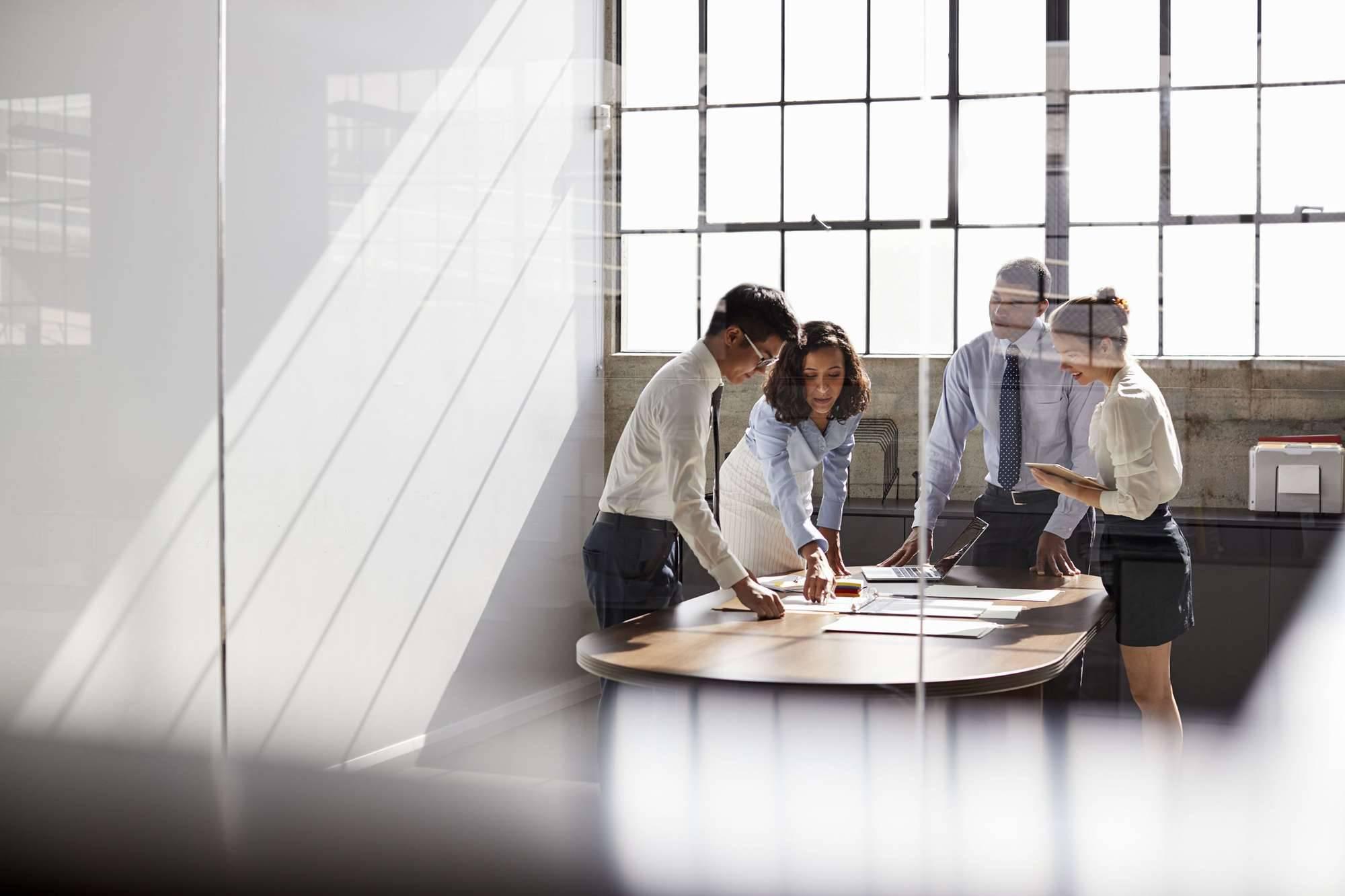 A group of four executives stand around a table looking at files and papers.