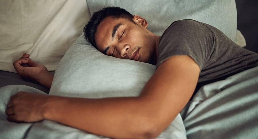A man sleeps in bed hugging a grey pillow.