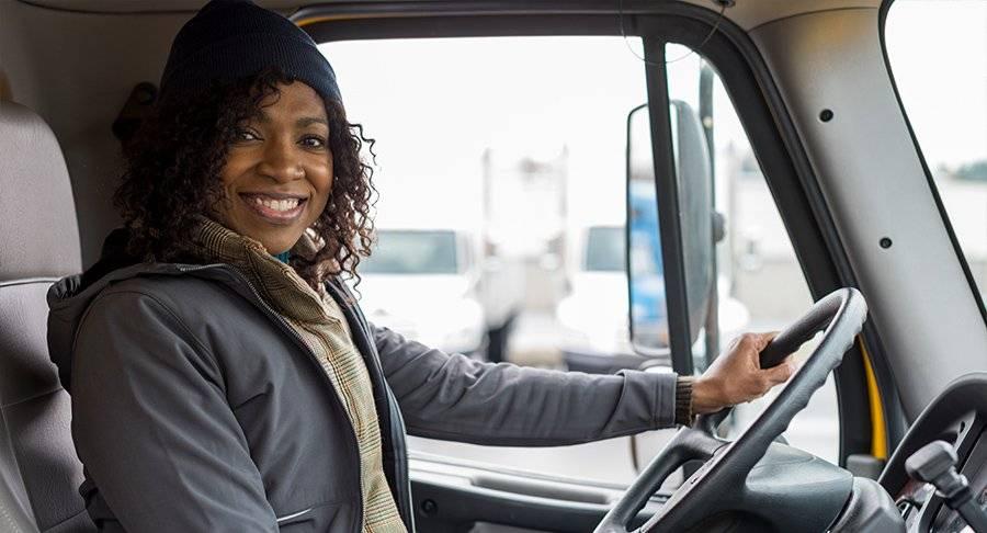 A smiling female driver sits behind the wheel of a truck.
