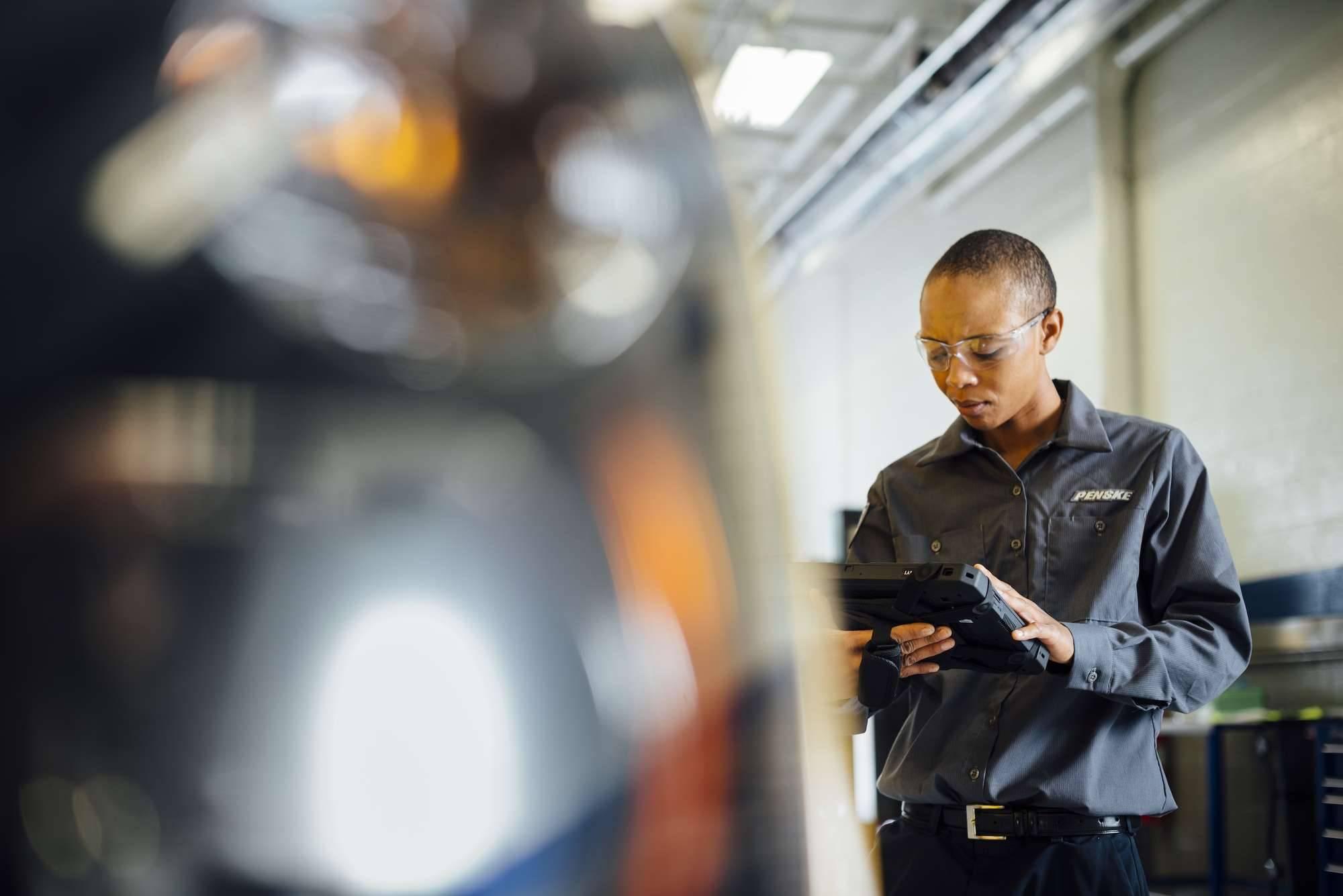 A technician looks at a handheld digital device while working on a semi-truck.