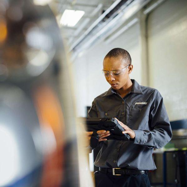 A technician looks at a handheld digital device while working on a semi-truck.
