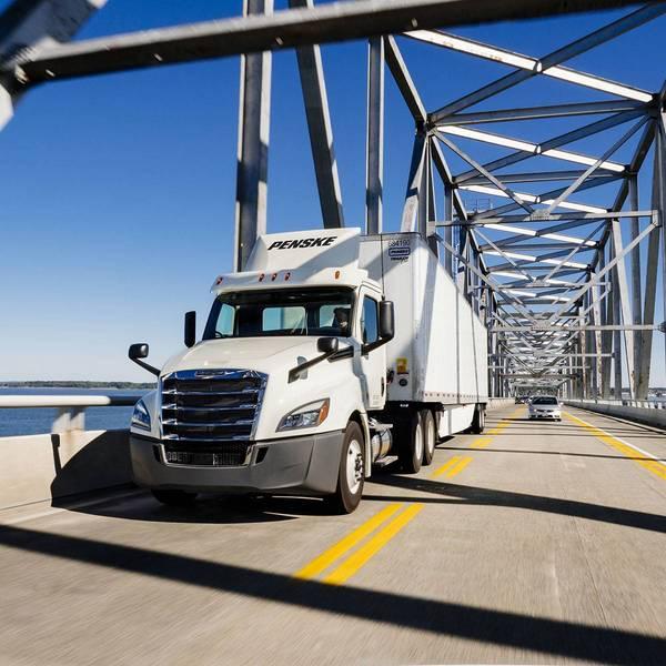 A white Penske semi-truck drives over a bridge.