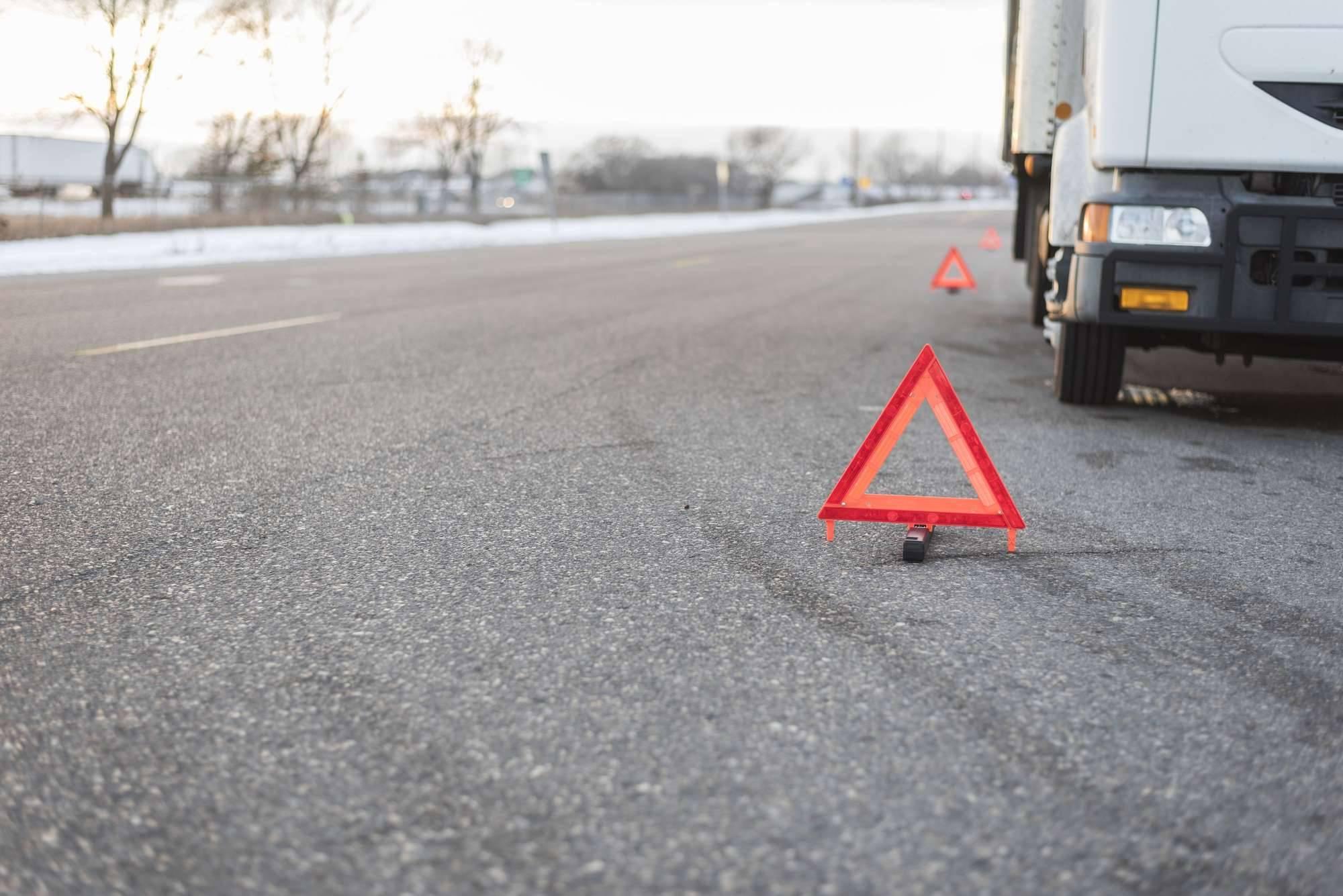 A white truck broken down on the side of the road surrounded by caution triangles.