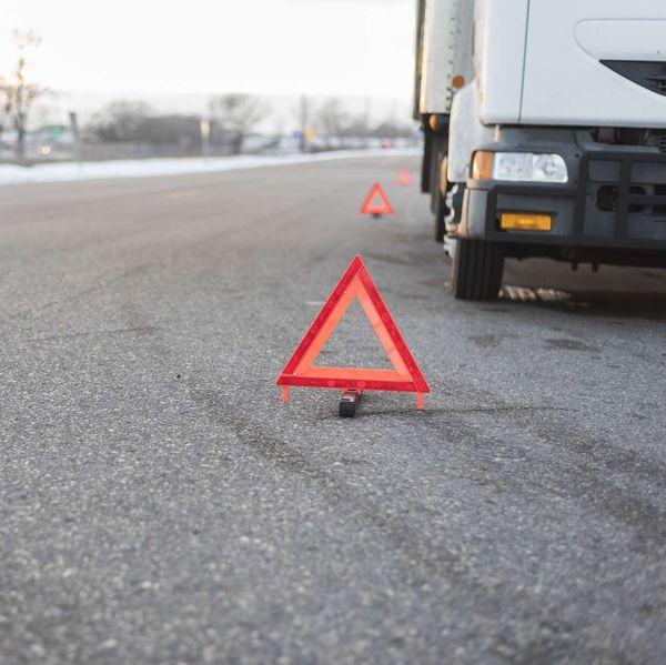 A white truck broken down on the side of the road surrounded by caution triangles.