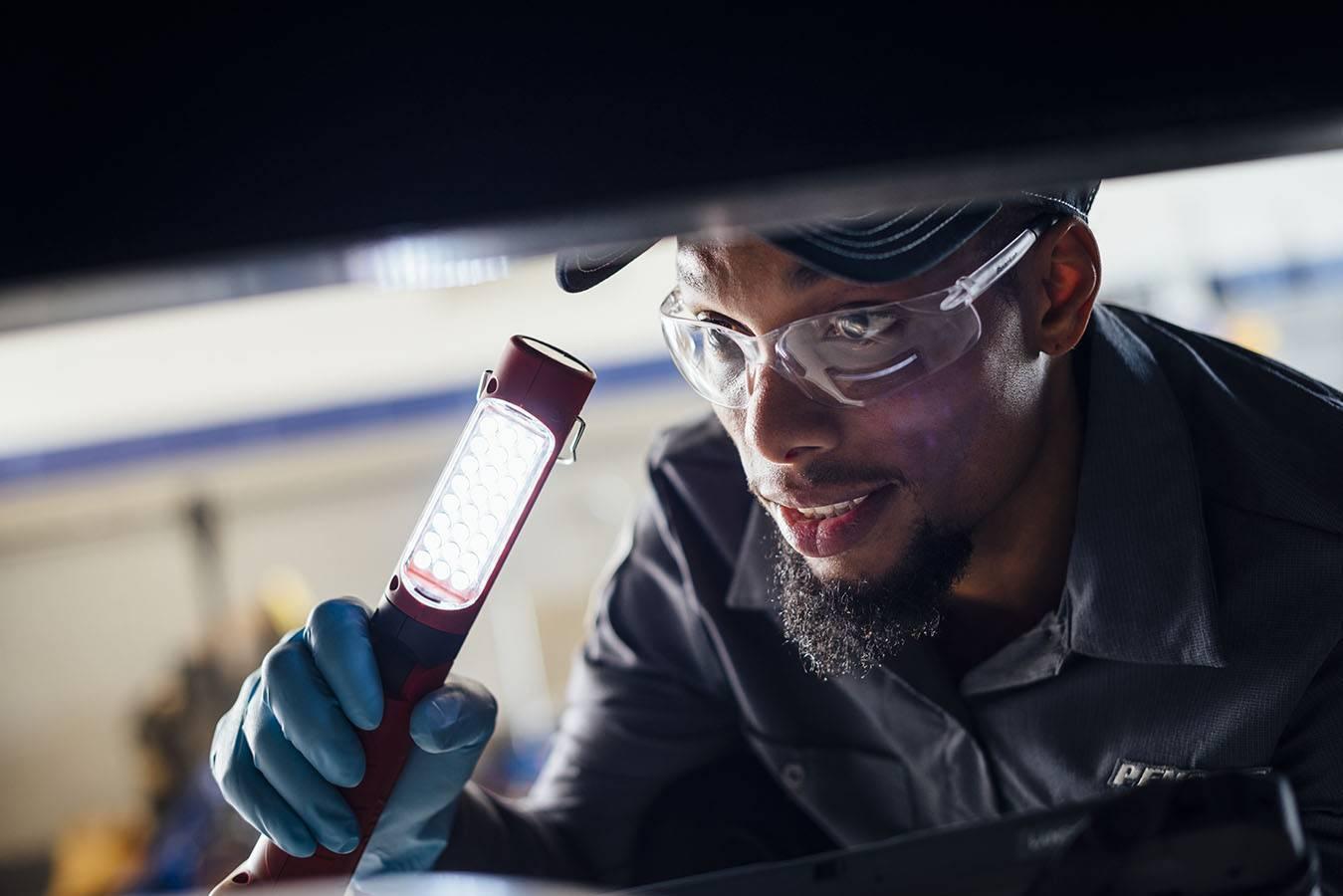Closeup of a maitenance technician holding a flashlight looking under a truck.