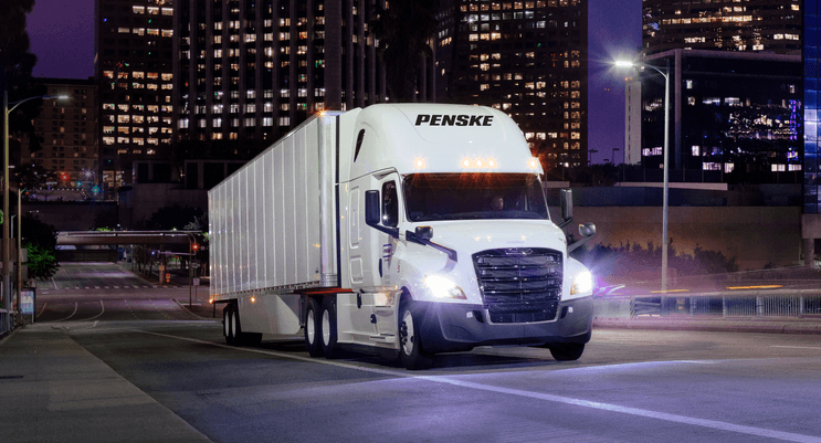 Penske tractor trailer driving through a city at night