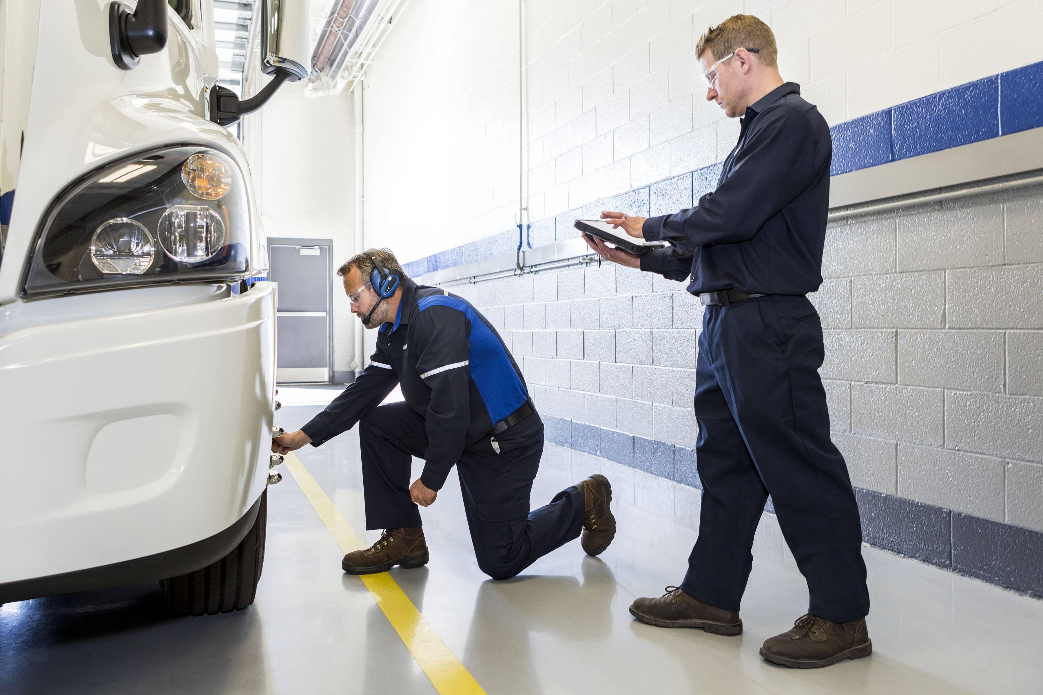 Two technicians check the alignment on a semi-truck wheel.